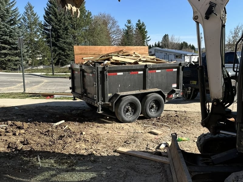 Bobcat excavator loading wood construction debris into black dump trailer