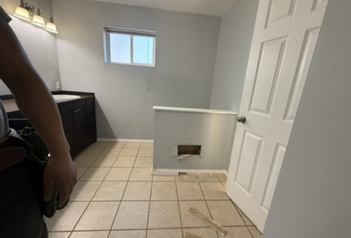 Bathroom before selective demolition — tile floor, vanity, and wall opening