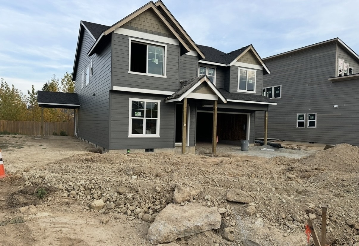 New home exterior mid-construction — dirt yard, no landscaping, unfinished garage